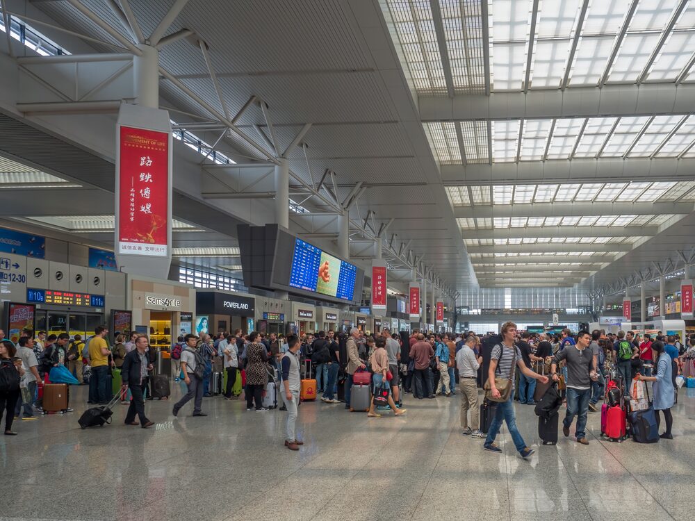 Crowded departure concourse of Shanghai Hongqiao Railway Station with gate signs overhead