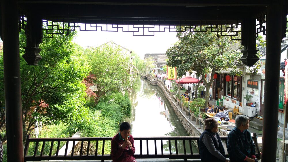 View down a Suzhou canal from under a covered bridge on Pingjiang Road, shops and trees on both banks