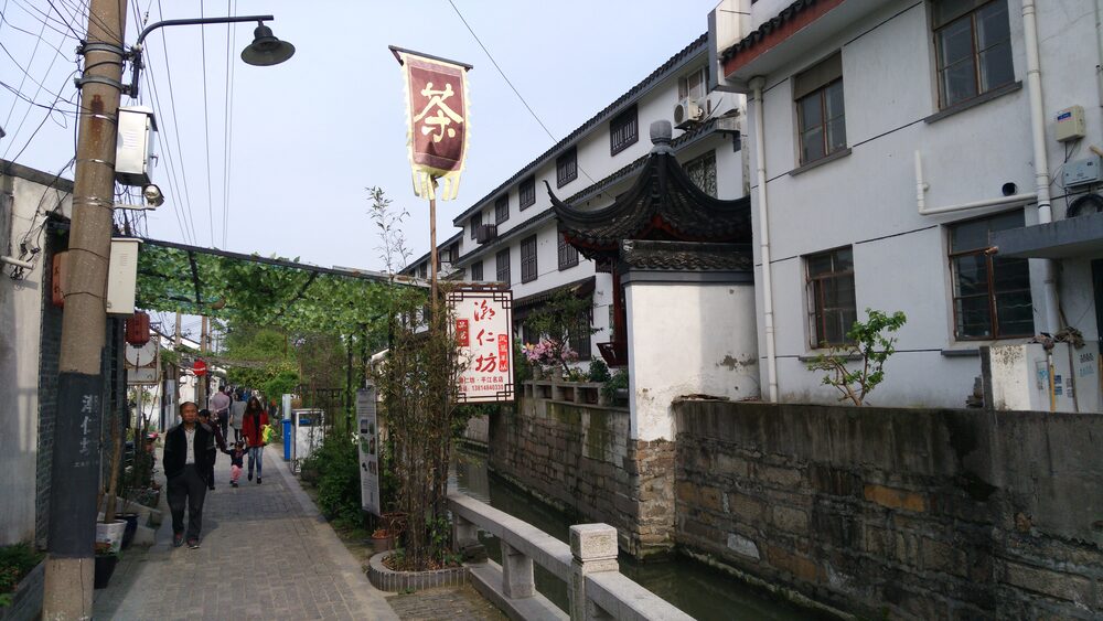 A narrow stone-paved lane on Pingjiang Road in Suzhou with whitewashed walls and a hanging shop banner