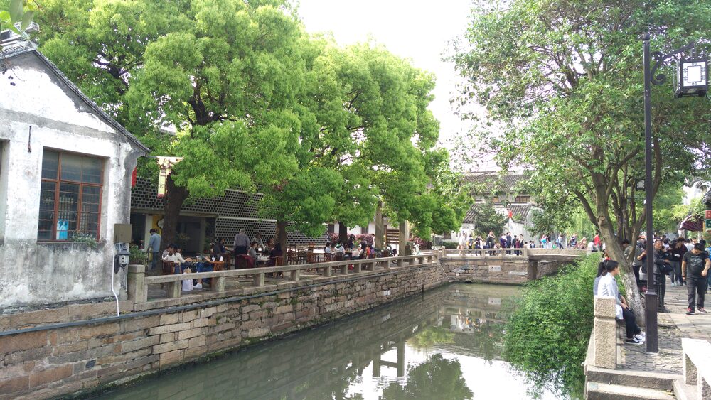 Canal-side walkway on Pingjiang Road in Suzhou with trees, low white houses and people walking