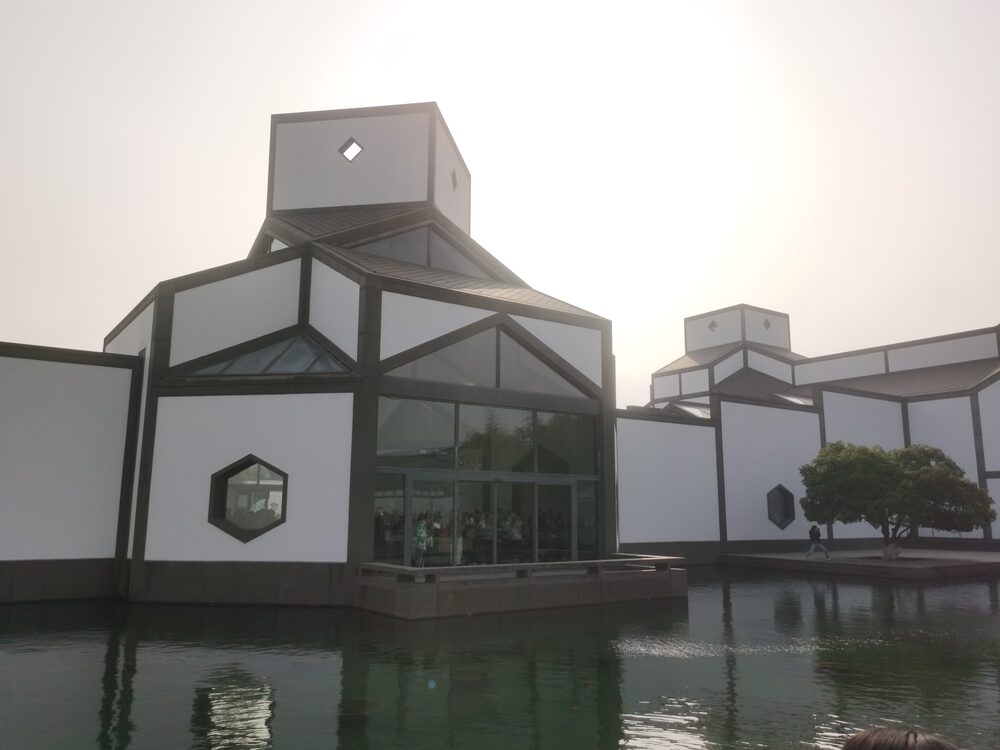 White walls and grey geometric roofs of the Suzhou Museum main building beside a pond
