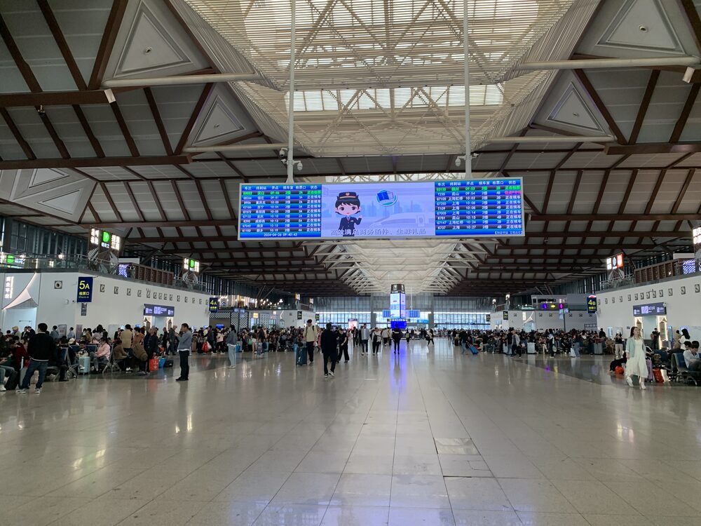 Large waiting hall of Suzhou Railway Station with a departures board under a traditional-style roof