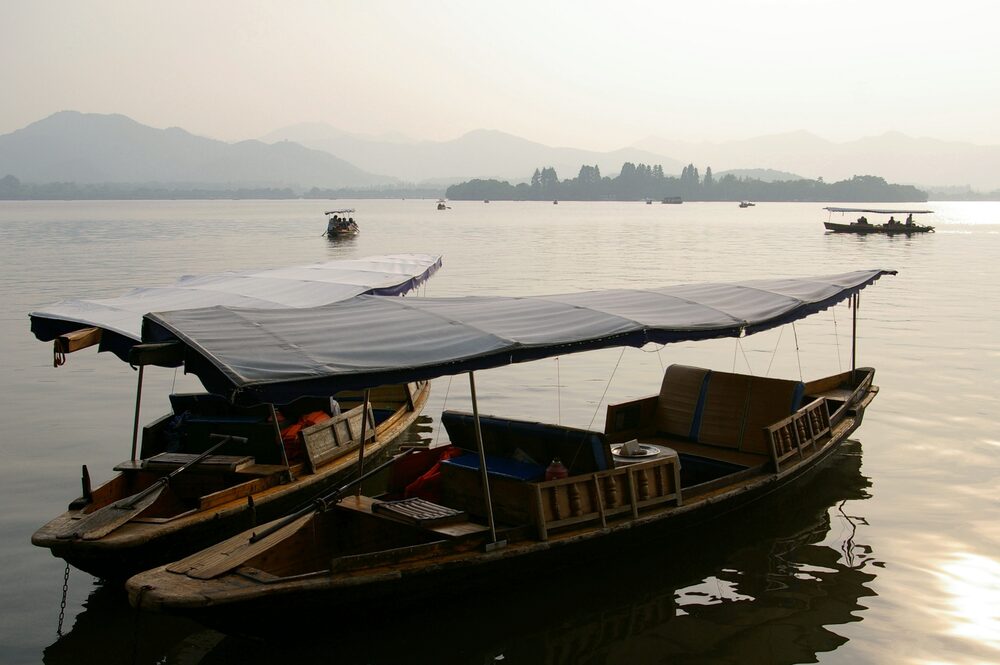 Wooden boats moored on West Lake in Hangzhou with hills behind them at sunset
